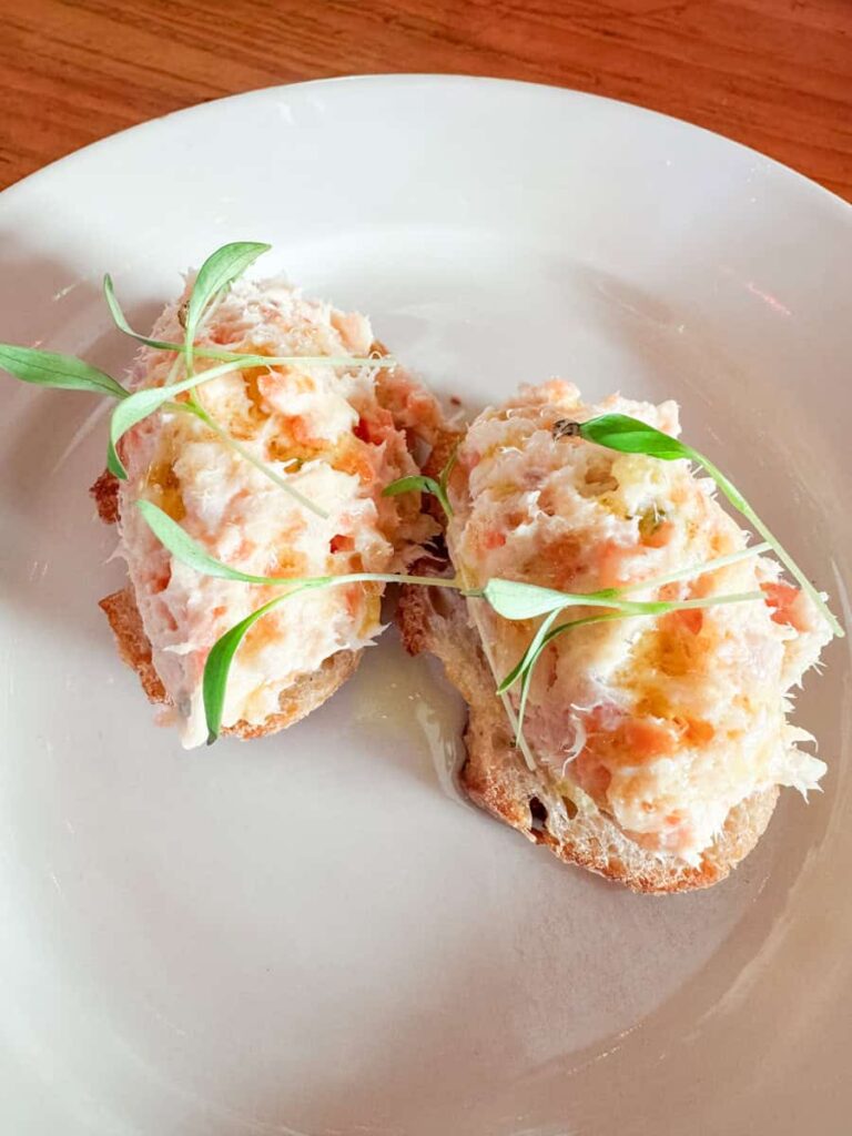 Two pieces of toasted bread topped with a smoked trout mixture and microgreens, served simply on a white plate.