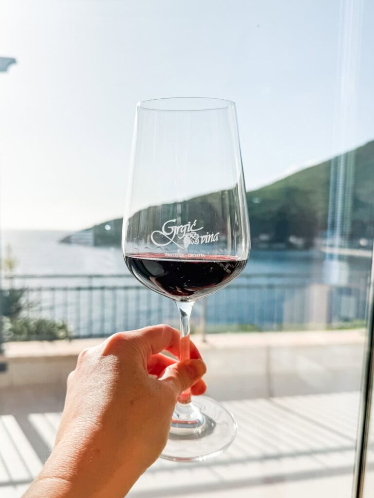 Glass of red wine at Grgić Vina overlooking the Adriatic Sea and coastal hills.