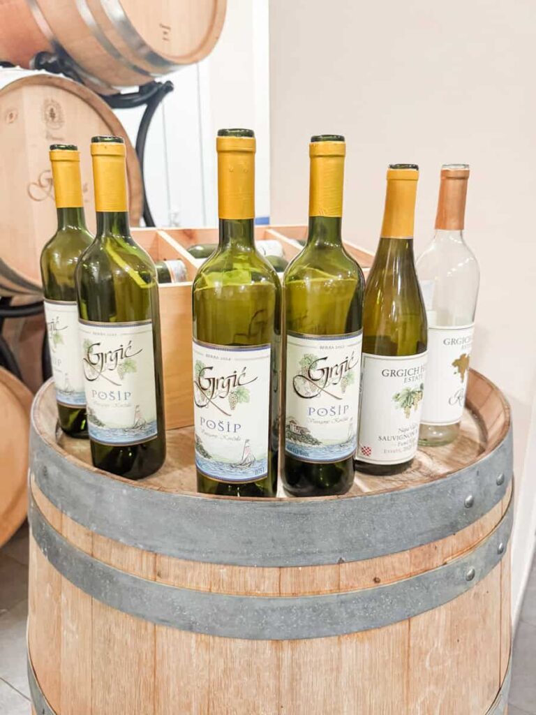 Bottles of Grgić Vina wines displayed on a wooden barrel inside the winery.