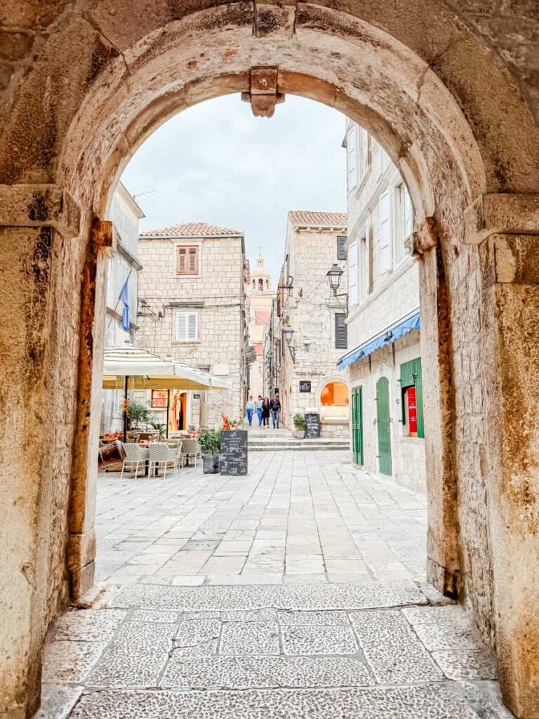 Stone archway framing a pedestrian street in Korčula Old Town, Croatia.