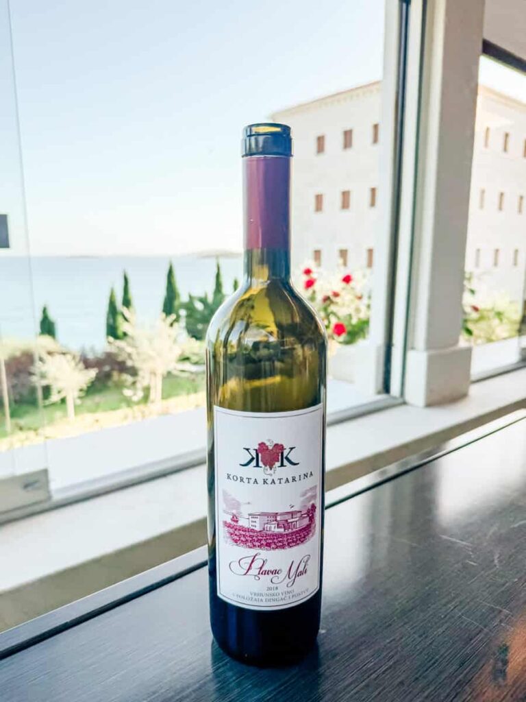 Bottle of Korta Katarina Plavac Mali wine displayed by a window overlooking the Adriatic Sea.