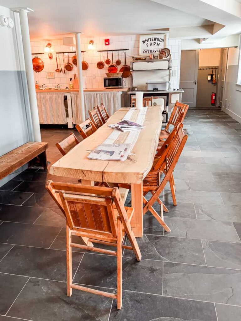 Cozy kitchen and breakfast dining area at the Boarding House with a long wooden table, hanging copper pots, and a sign reading “Whitewood Farm Oysterville.”