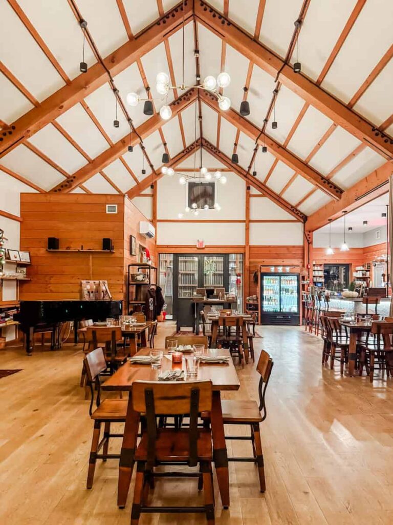 Warm, wood-accented dining room with vaulted ceilings, a grand piano, and tables set for service.