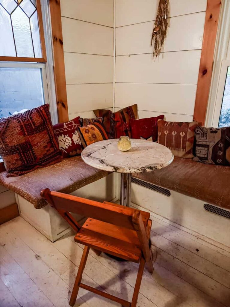 Corner bench with patterned pillows and a small round marble table inside Sunshine Colony wine bar, creating a warm and inviting atmosphere.