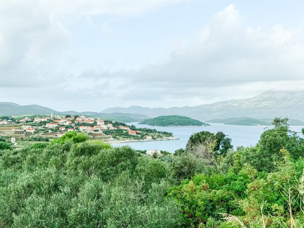 View of Lumbarda village on Korčula Island, with red-roofed houses, olive groves, and the Adriatic Sea stretching toward nearby islets and mountains.