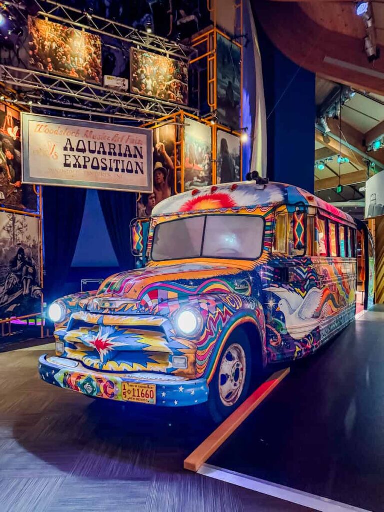 Brightly painted retro bus with psychedelic designs and glowing headlights, displayed at the Bethel Woods museum's Woodstock exhibit.