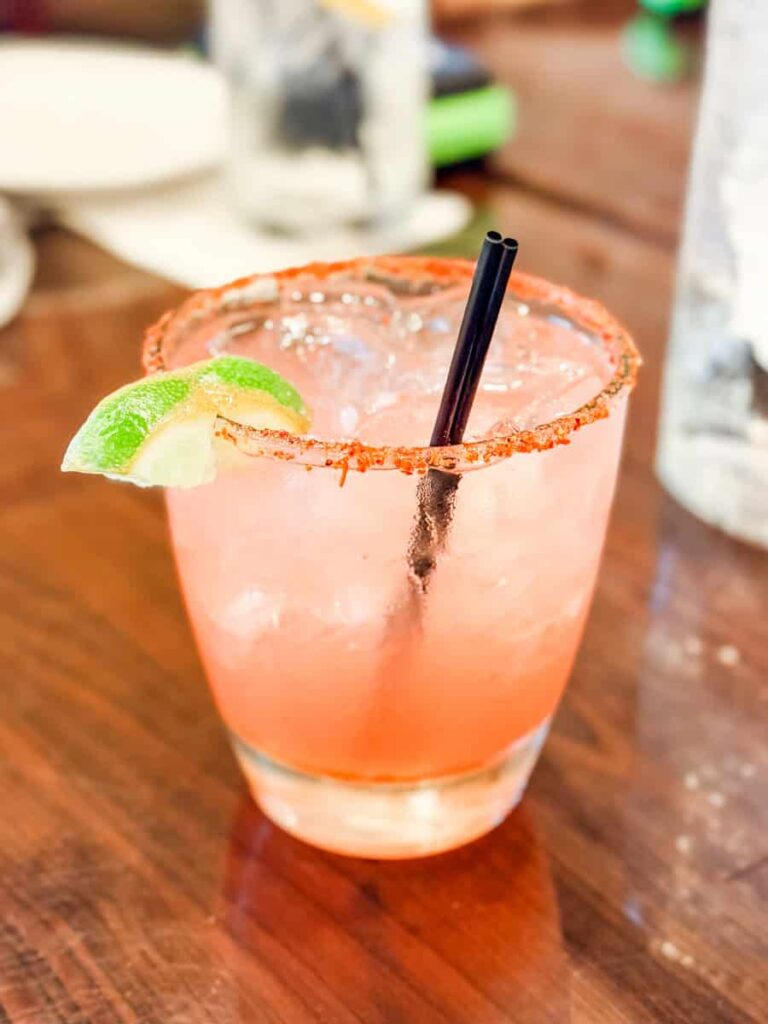 Pink cocktail with a chili salt rim, lime wedge, and ice served at Golden Leaf Bistro.