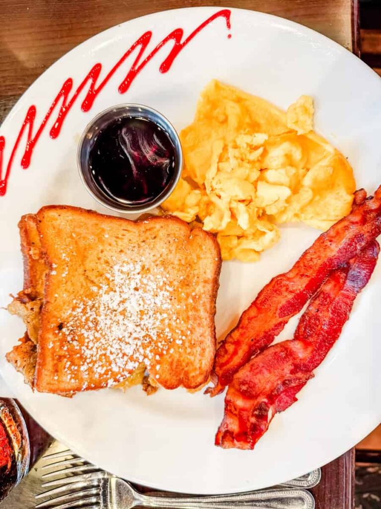 Brunch plate with stuffed French toast, scrambled eggs, crispy bacon, and a side of syrup at Golden Leaf Bistro.