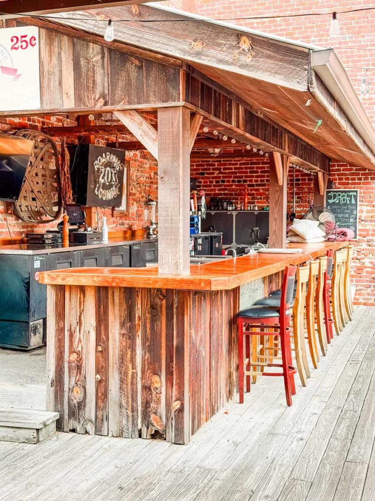 Covered outdoor bar with wooden counters, high-top stools, and exposed brick walls at Golden Leaf Bistro.