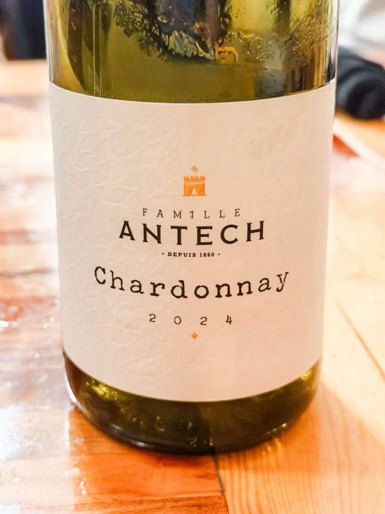 Bottle of Famille Antech Chardonnay 2024 on a wooden table at King Cropp Kitchen. The label reads "Famille Antech Chardonnay 2024."
