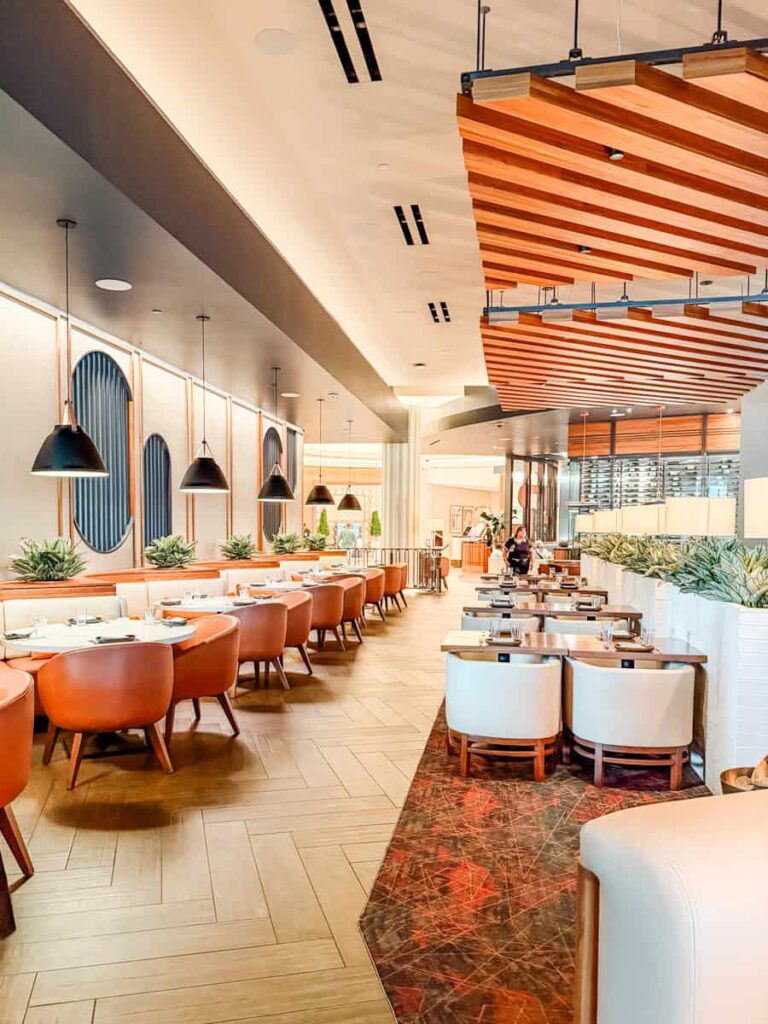 Modern dining room at Ramsay's Kitchen with wood ceiling accents, leather chairs, and rows of neatly set tables.