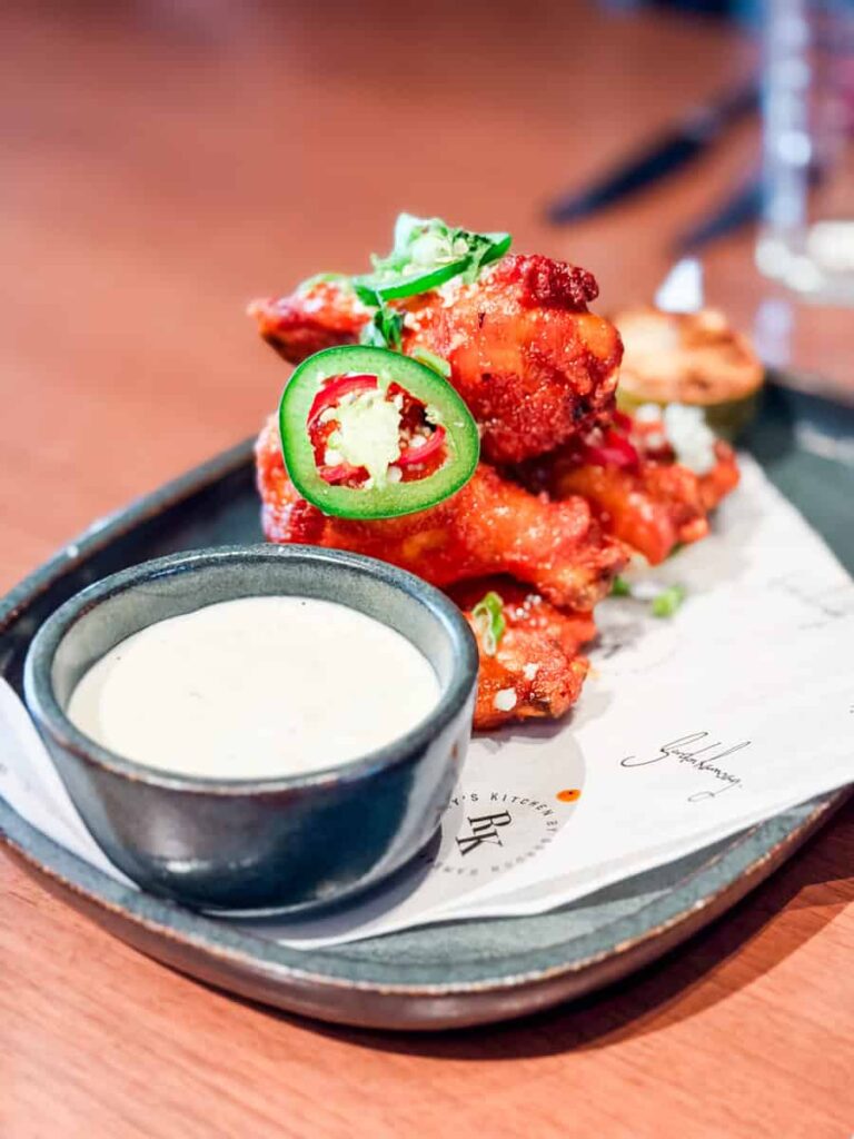 Crispy chicken wings topped with sliced jalapeños and green onions served with a side of dipping sauce at Ramsay's Kitchen.