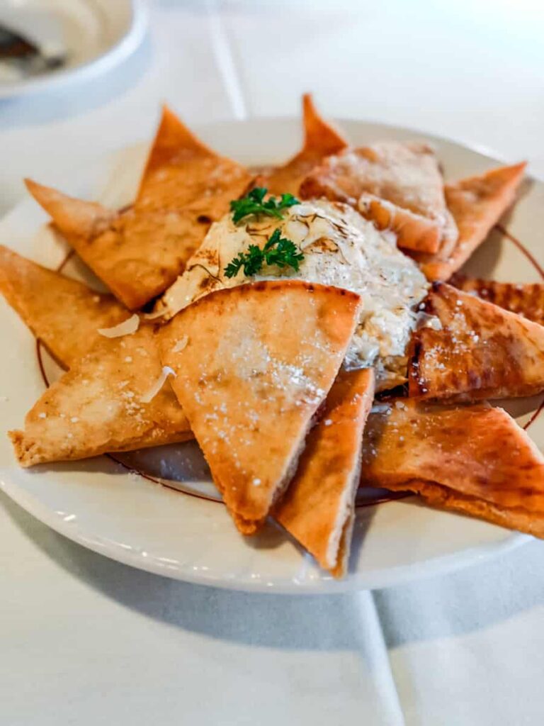 Toasted pita triangles surround a creamy crab dip topped with herbs on a white plate at The Schoolfield Restaurant in Danville.