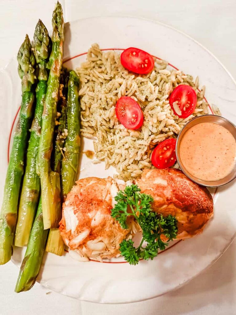 Two golden crab cakes are served with roasted asparagus, seasoned rice, cherry tomatoes, and a creamy sauce at The Schoolfield Restaurant in Danville.