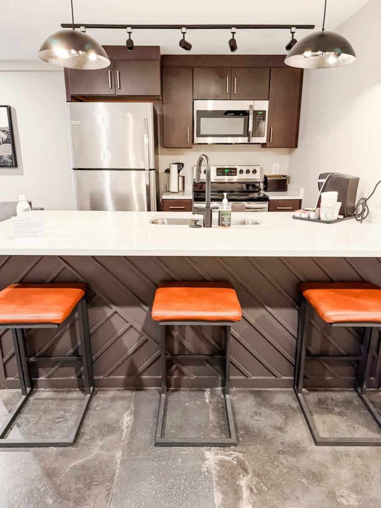 Modern suite kitchen at The Bee featuring an island, stainless steel appliances, and three leather bar stools.