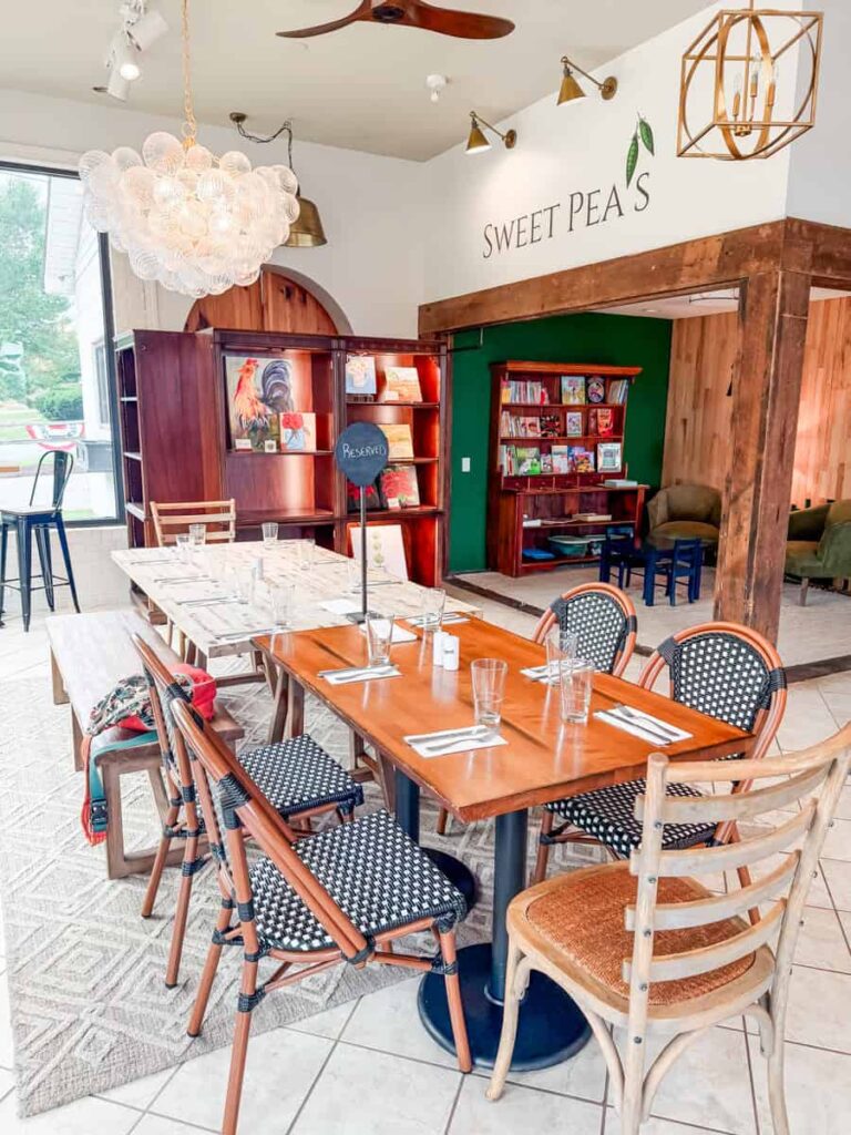 Bright dining room at The Pod restaurant in Gretna with wood accents, modern lighting, communal tables, and a cozy reading nook in the background. Text on the wall reads "SWEET PEA'S."