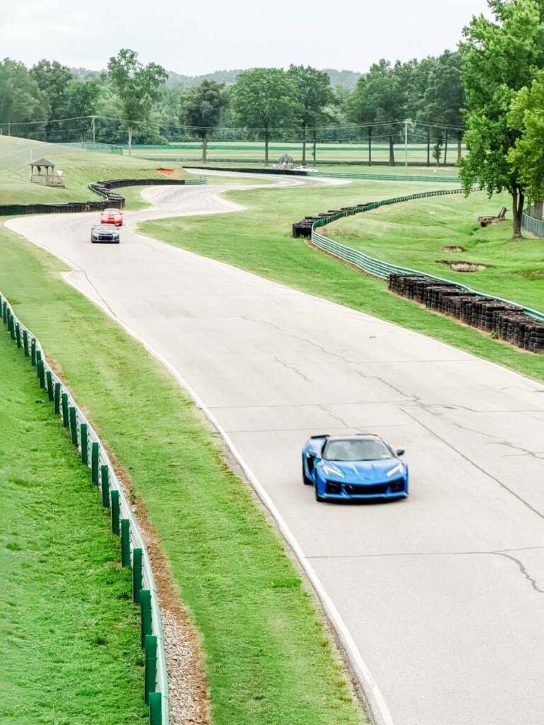 Sports cars drive along the winding road course at Virginia International Raceway with rolling green hills and safety barriers lining the track.