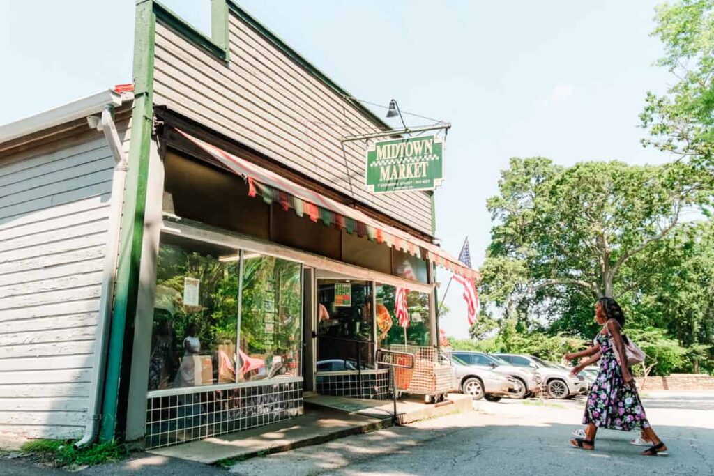 Exterior of Midtown Market in Danville with vintage storefront, striped awning, and American flags as two women walk toward the entrance on a sunny day. The hanging sign reads "Midtown Market."